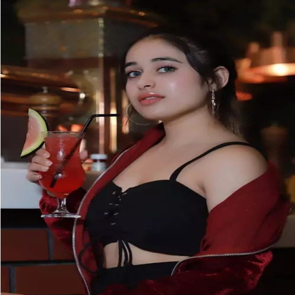 A GIRL SEXY LOOKS 24 YEARS OLD NAME IS MAMTA WEARING MAROON JACKET AND BLACK DRESS TAKING JUSE ON HER HAND IN STANDING POSITION